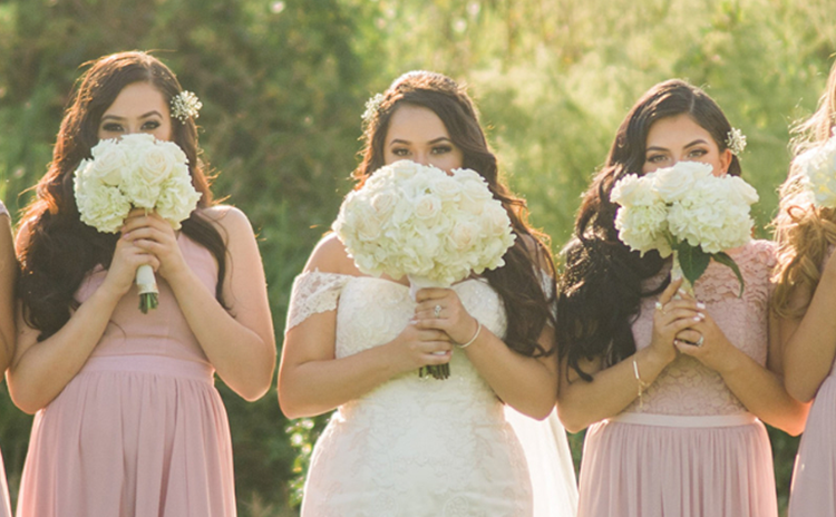 Bridal party wearing pink dresses with bride while holding white bouquets